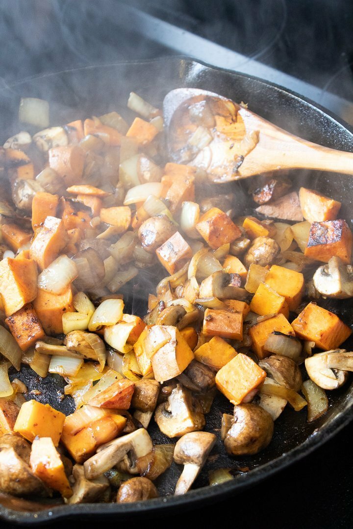 Onions, yam and mushrooms sautéing in a cast iron skillet.