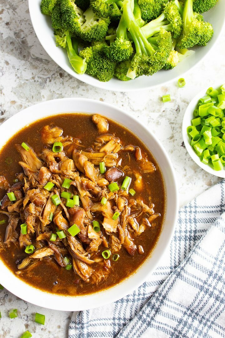 Overhead shot of Easy AIP Crockpot Chicken Teriyaki in a white bowl, topped with green onions and served with broccoli.