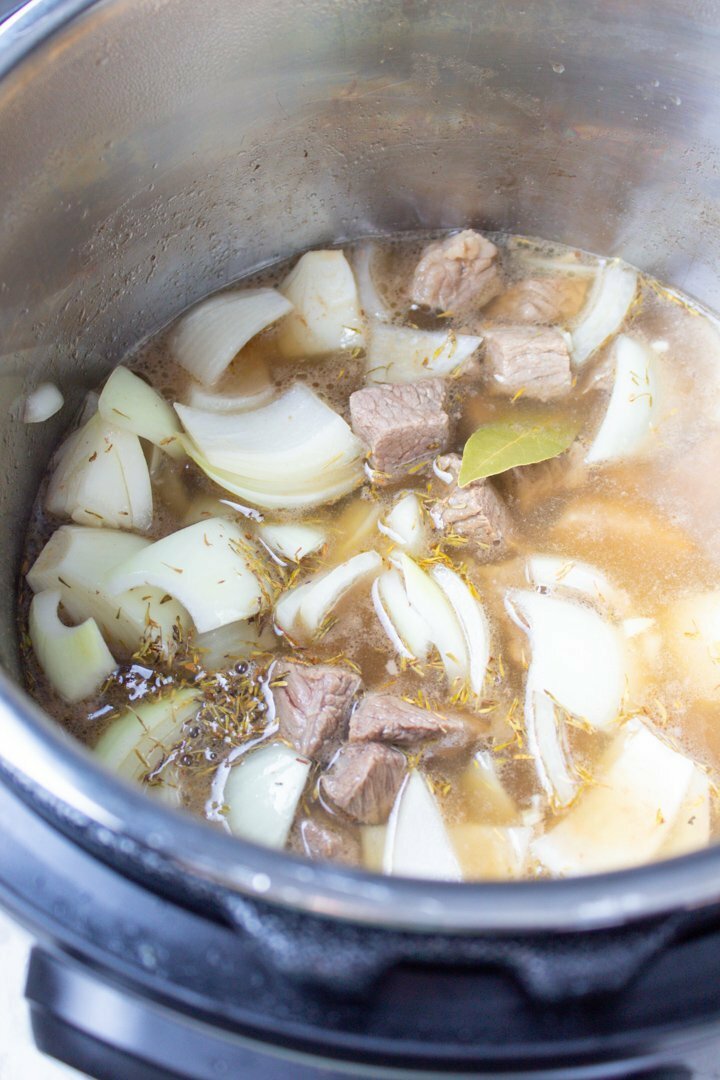 Detail shot of stew beef, onions, garlic, spices and broth in an Instant Pot.